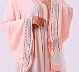 Woman wearing a light pink abaya with a matching headscarf on a white background